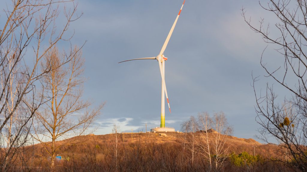 Windkraftanlage auf einer Anhöhe vor blauem Himmel