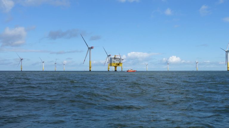 Offshore-Windturbinen und eine Umspannplattform in der Nordsee, davor ein orangefarbenes Versorgungsschiff.
