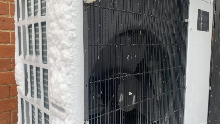 Außeneinheit einer Luft-Wasser-Wärmepumpe an einer Hauswand im Schnee